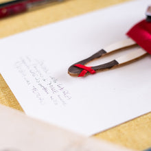 Carica l'immagine nel visualizzatore di Gallery, Dettaglio dell'ANGELO della LAUREA in legno di pioppo dipinto e vestito a mano, abito di cotone rosso con maniche in nastro color tortora. Coccinella e libricini sagomati in carta; piccolo fiocco di raso rosso sulla scarpetta.