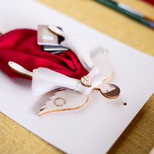 Carica l'immagine nel visualizzatore di Gallery, Dettaglio dell'ANGELO della LAUREA in legno di pioppo dipinto e vestito a mano, abito di cotone rosso con maniche in nastro color tortora. Coccinella e libricini sagomati in carta; piccolo fiocco di raso rosso sulla scarpetta.