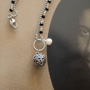 Dettaglio del bracciale CUORE con due fili ad incatenato, uno con perle di agata nera ed uno con palline argentate, ed un cuore in metallo lavorato.