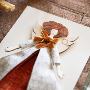 Dettaglio dell'ANGELO dei TRAGUARDI IMPORTANTI, struttura in legno dipinta e vestita a mano, abito in gobelin color bianco con fantasia floreale, gonna in cotone color arancio scuro e fiocco in velluto color ruggine. 
