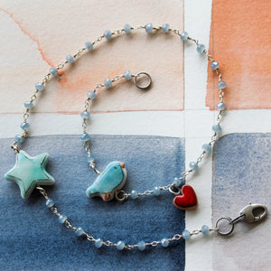 bracciale a doppio giro con incatenato a rosario di cristalli azzurri, piccolo uccellino azzurro con stella e cuoricino rosso in ceramica fatti a mano