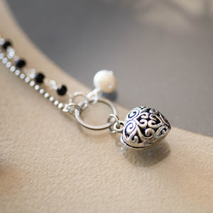 Dettaglio del bracciale CUORE con due fili ad incatenato, uno con perle di agata nera ed uno con palline argentate, ed un cuore in metallo lavorato.