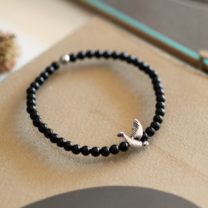 Bracciale RONDINE elastico con perle di agata nera e piccola rondine in metallo.