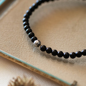 Dettaglio del bracciale RONDINE elastico con perle di agata nera e piccola rondine in metallo.