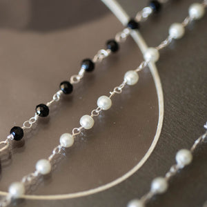 Dettaglio della collana CUORE con un charm a forma di cuore lavorato, catene con perline in vetro nero e bianco perla ad incatenato, perle piatte di madreperla nera.