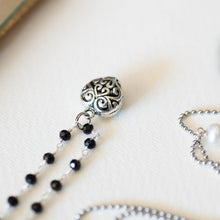 Carica l&#39;immagine nel visualizzatore di Gallery, Dettaglio della collana CUORE con un charm a forma di cuore lavorato, catene con perline in vetro nero e bianco perla ad incatenato, perle piatte di madreperla nera.
