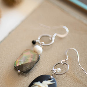 Dettaglio degli orecchini CAMEO asimmetrici con charm a forma di cammeo in resina color nero e avorio, perla piatta di madreperla nera e cristallini neri e piccole perline bianche.