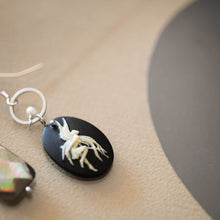 Load image into Gallery viewer, Dettaglio degli orecchini CAMEO asimmetrici con charm a forma di cammeo in resina color nero e avorio, perla piatta di madreperla nera e cristallini neri e piccole perline bianche.
