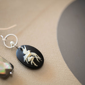 Dettaglio degli orecchini CAMEO asimmetrici con charm a forma di cammeo in resina color nero e avorio, perla piatta di madreperla nera e cristallini neri e piccole perline bianche.