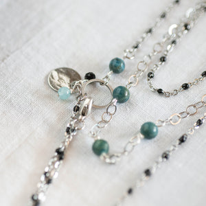 Dettaglio della collana DOPPIA medio-lunga a due fili, realizzata con catene color argento, perle di apatite grezzo scuro e catena a rosario con cristalli neri.