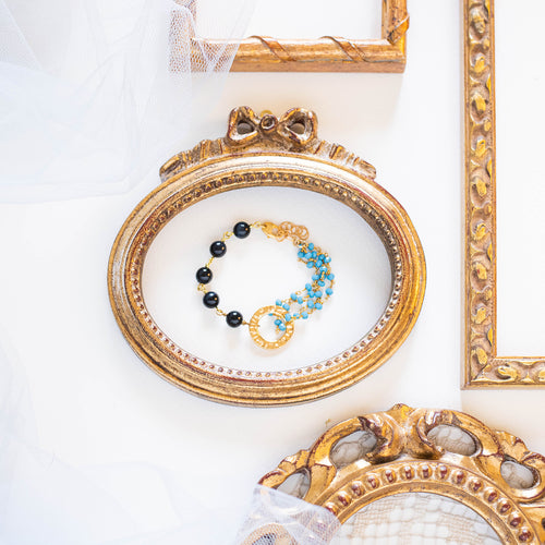 Bracciale ROSARIO realizzato per metà con un incatenato di perle di occhio di tigre blu e per l'altra metà con una catena a rosario con cristalli turchesi; elemento centrale dorato a forma di cerchio.