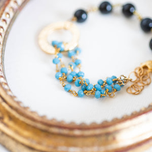 Dettaglio del bracciale ROSARIO realizzato per metà con un incatenato di perle di occhio di tigre blu e per l'altra metà con una catena a rosario con cristalli turchesi; elemento centrale dorato a forma di cerchio.