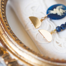 Load image into Gallery viewer, Dettaglio degli orecchini CAMEO BLU asimmetrici con charm a forma di cammeo in resina color blu e avorio, perle di lapislazzulo tinto blu satinato e charm dorato.
