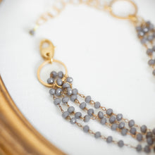 Load image into Gallery viewer, Dettaglio del bracciale FILI realizzato con fili di cristalli grigi montati a rosario ed un elemento centrale tondo dorato.
