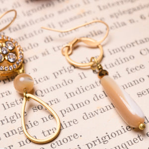 Dettaglio degli orecchini QUADRIFOGLIO asimmetrici con un elemento metallico tondo con struttura interna a forma di quadrifoglio con zirconi sfaccettati ed incastonati, goccia pendente e perlina in madreperla cappuccino.